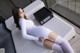 A woman in a white bodysuit and stockings laying on a couch.