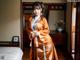 A woman in an orange kimono standing in a bedroom.