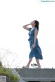 A woman in a blue dress standing on a concrete ledge.