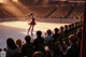 A woman in a red dress skating on an ice rink in front of a crowd.