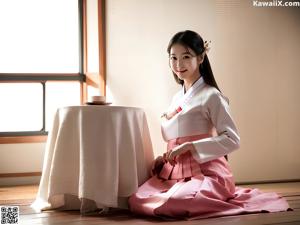 A woman in a pink kimono sitting on the floor next to a table.