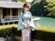 A woman in a blue and pink kimono standing in front of a pond.