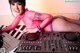 A woman in a pink bodysuit sitting next to a dj mixer.